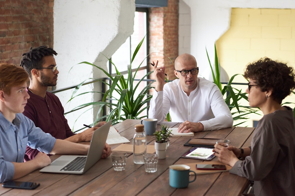 An office team meet together around a table. 